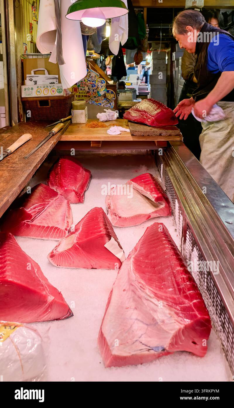 Ein Fischhändler bereitet ein Stück rohen Thunfisch auf einer Holzplatte hinter Fischblöcken vor, die auf zerkleinertem Eis gekühlt sind, auf dem Tokyo Fish Market Stockfoto