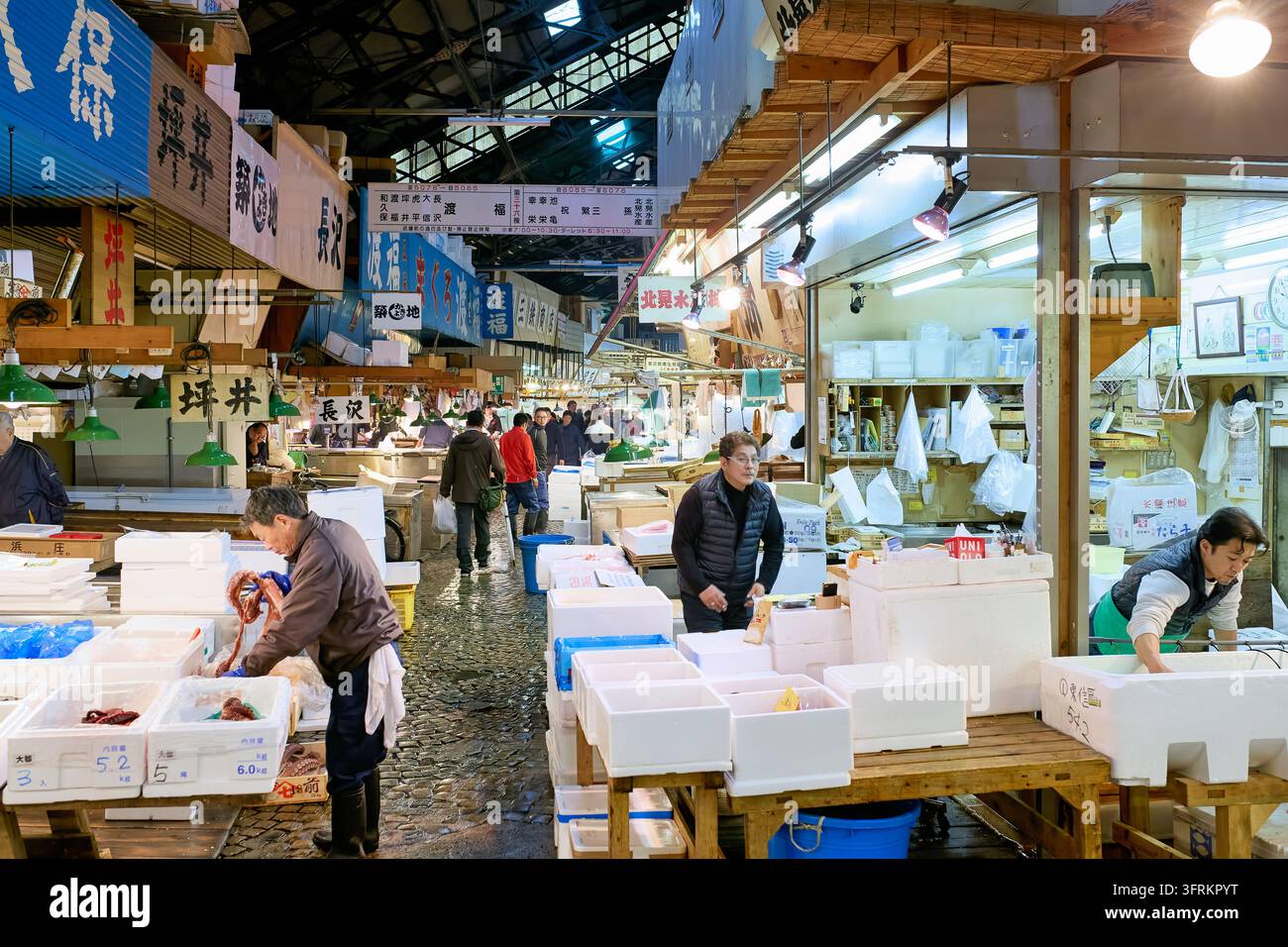 Fischhändler bearbeiten Tintenfisch und sortieren Meeresfrüchte in Polystyrolboxen entlang eines nassen Kopfsteinpflastergangs des alten Großmarktes in Tokio, Japan Stockfoto