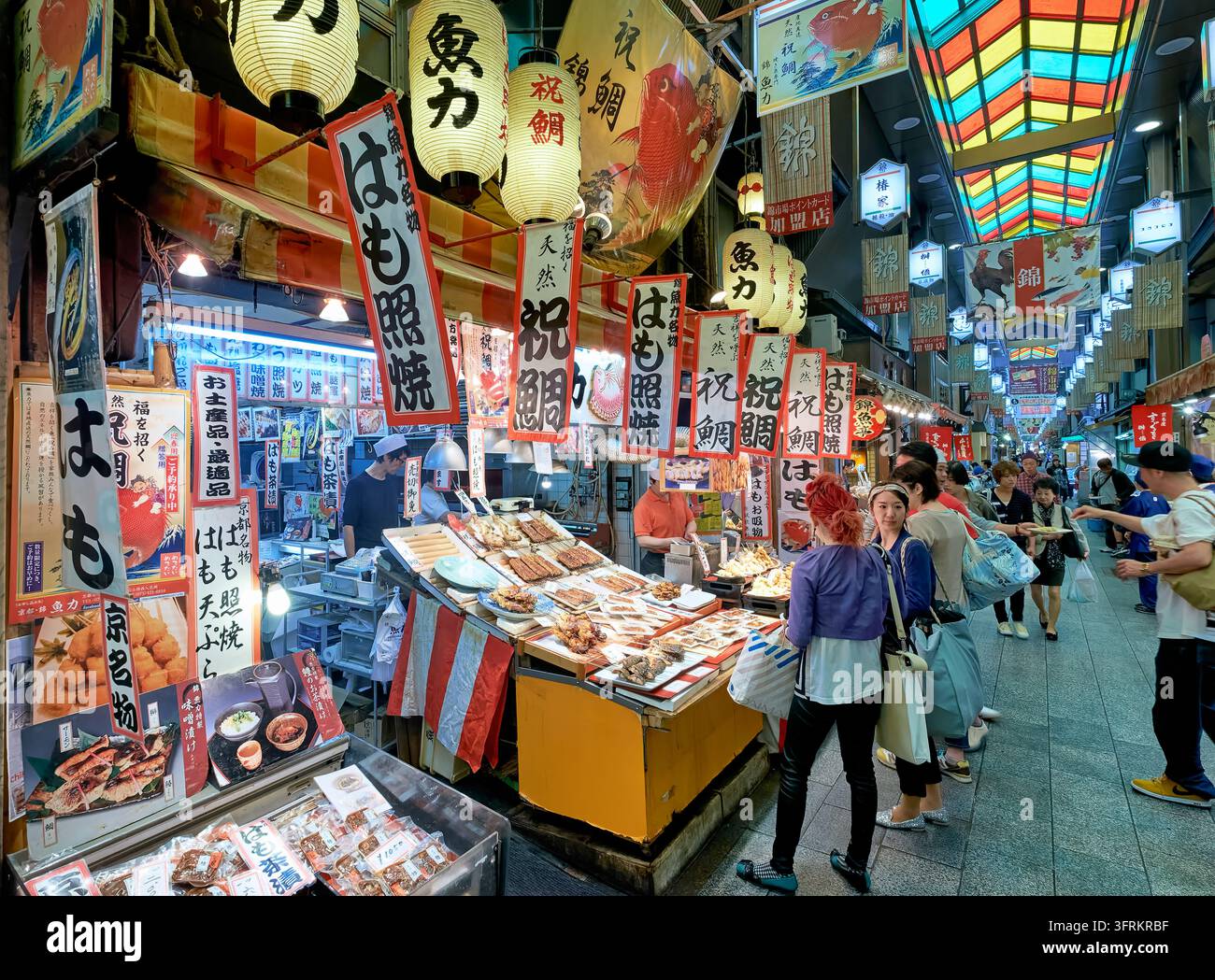 Einkäufer durchstöbern einen Stand, der gegrillten Aal und Seebarsch unter Papierlaternen in einer überdachten Essensarkade im Zentrum von Kyoto anbietet. Stockfoto