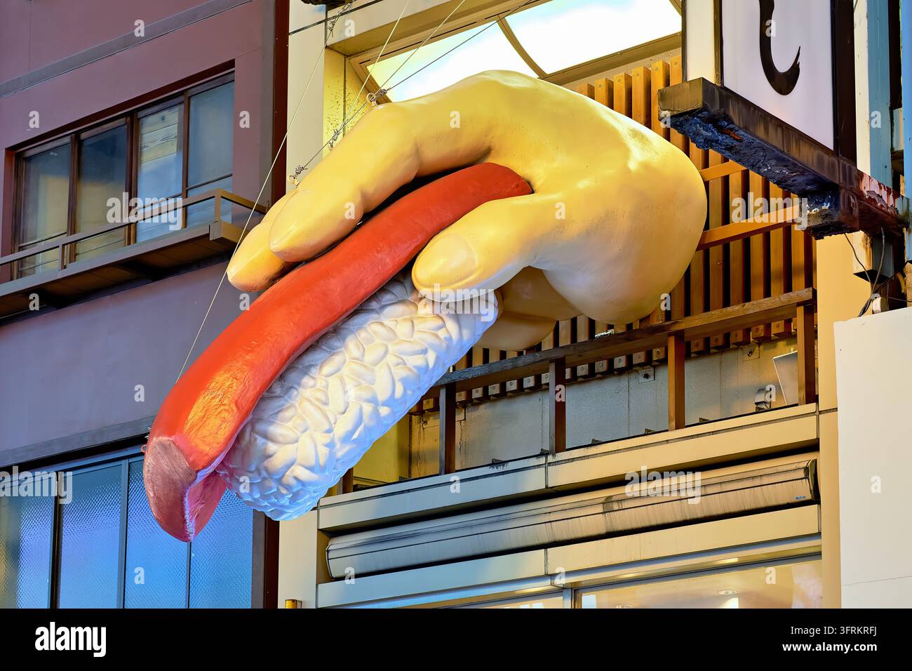 Übergroßer geformter Faust, der eine Scheibe Thunfisch auf Reis hält, hängt über einer Restaurantfassade in Japan in der Dämmerung. Stockfoto