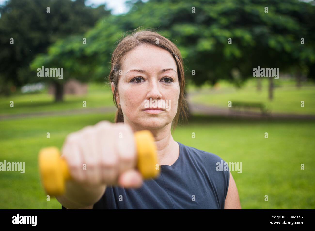 Nahaufnahme-Porträt einer konzentrierten Frau, die ihren Arm nach vorne streckt, während sie eine gelbe Hantelstange während einer Outdoor-Widerstandstraining-Übung in einer Kneipe hebt Stockfoto