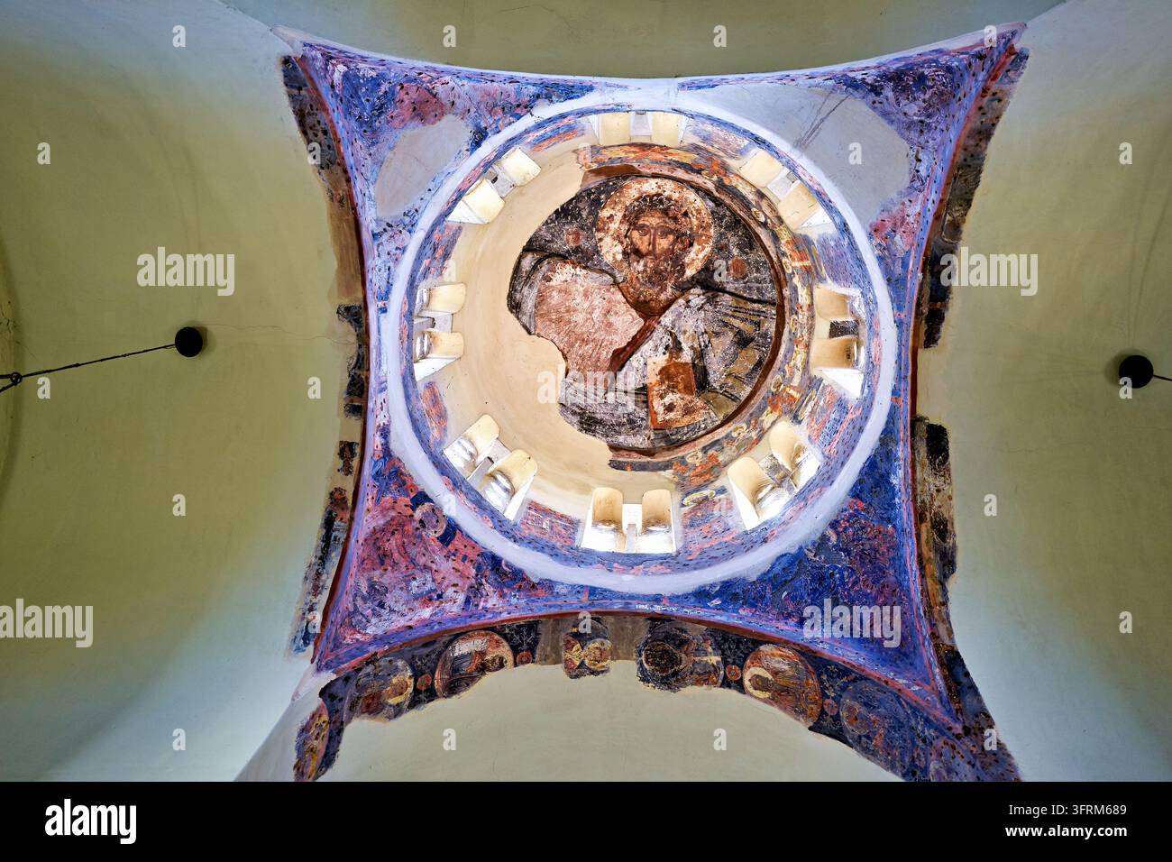 Niedrigwinkelaufnahme einer bemalten orthodoxen Kuppel mit Christus, der die Evangelien hält, umgeben von Fenstern und verblassten Fresken an den Pendentifs, Athen, Griechenland. Stockfoto