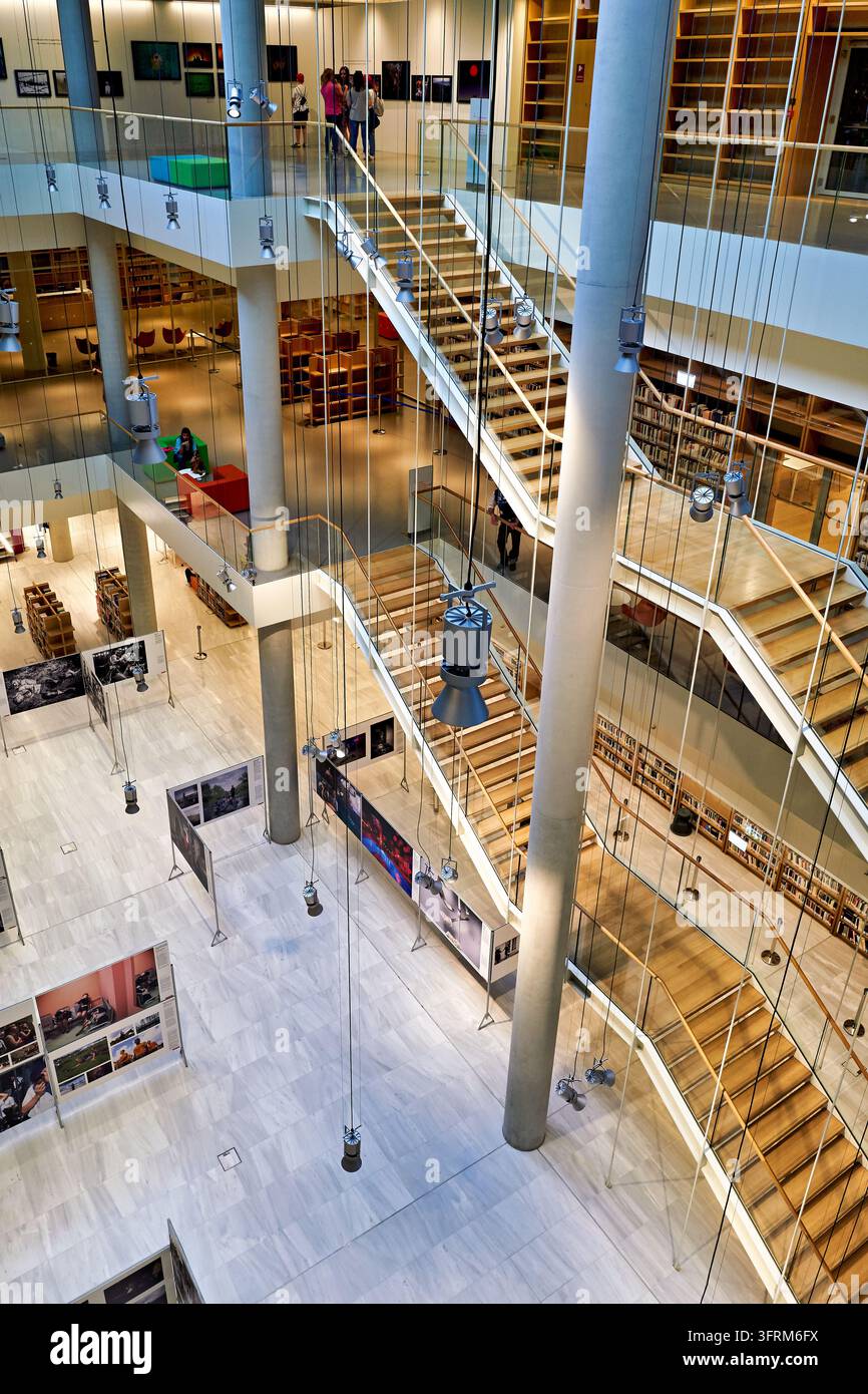 Holztreppen, Glasgeländer und hängende Spotlichter erheben sich durch ein mehrstöckiges Bibliotheksinnere, das eine Fotografieausstellung beherbergt Stockfoto