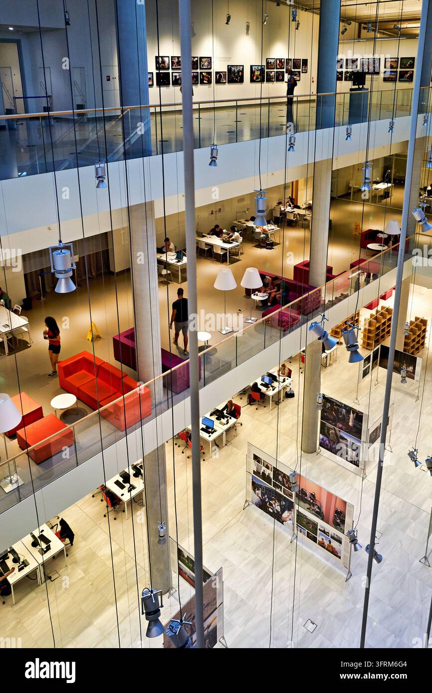 Besucher studieren an Schreibtischen und entspannen sich auf roten Sofas über einer Fotoausstellung im Kulturzentrum der Stavros Niarchos Foundation Stockfoto