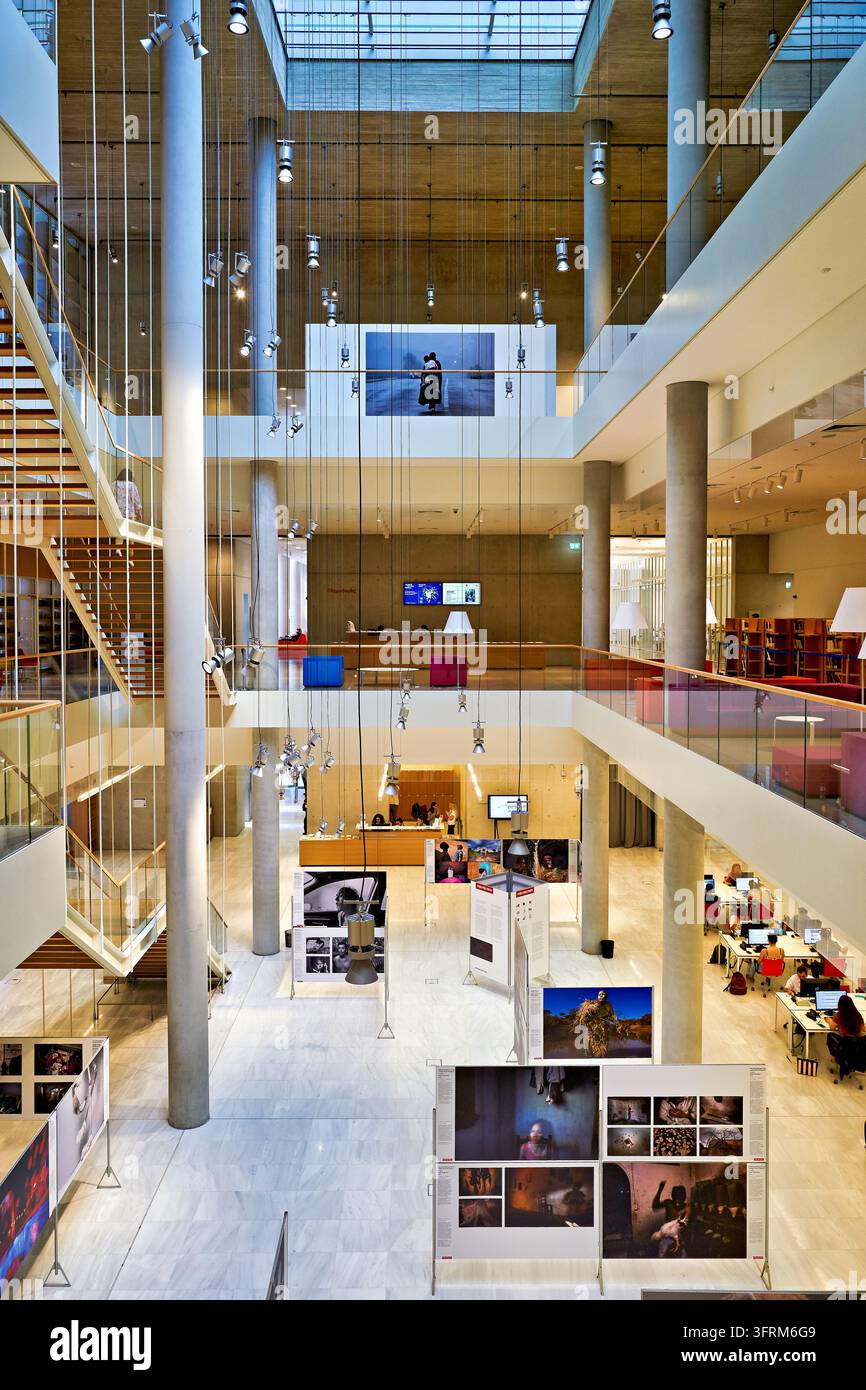 Mehrstöckiges Atrium mit hängenden Scheinwerfern, Treppe und Lesetischen, das eine Fotojournalismus-Ausstellung in einer öffentlichen Bibliothek beherbergt Stockfoto