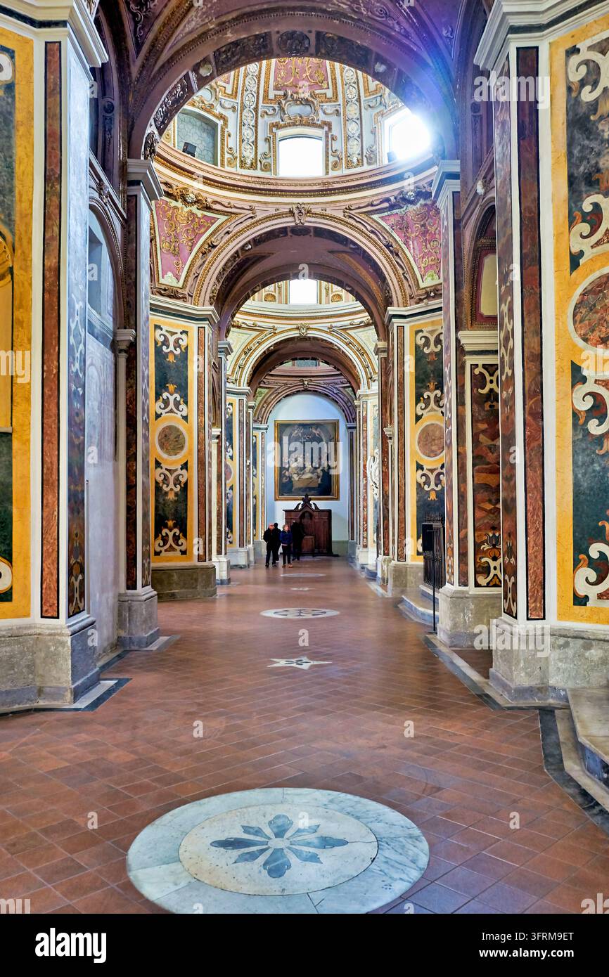 Barockes Interieur mit polychromen Pilastern, vergoldeten Stuckkuppeln und Terrazzoboden; entfernte Besucher in der Nähe eines Altarbildes. Stockfoto