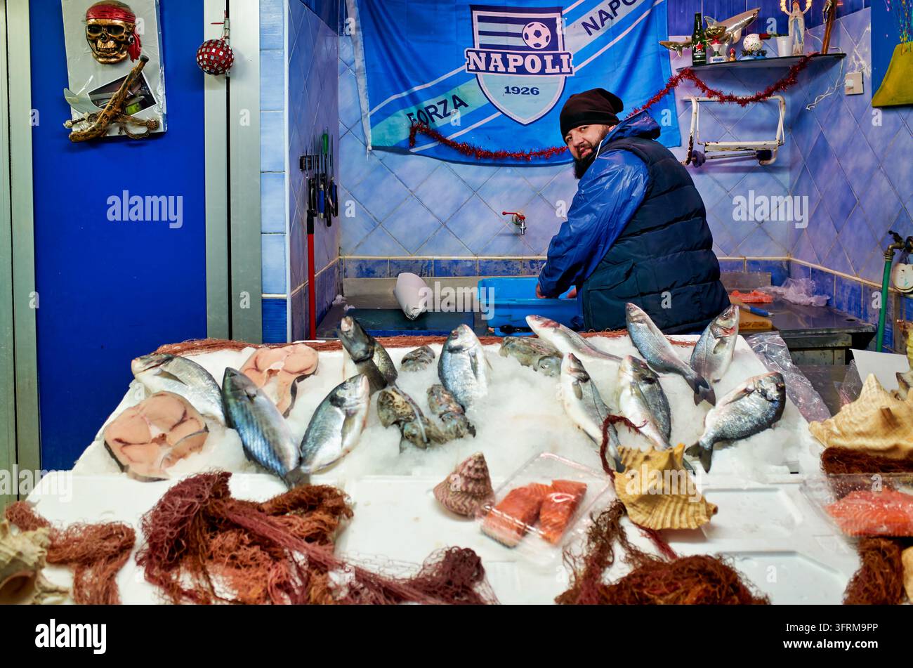 Bärtiger Händler arbeitet hinter einer Theke mit Brassen, Schwertfischsteaks und Lachs in einem blau gekachelten Geschäft, Neapel, Kampanien, im Winter Stockfoto