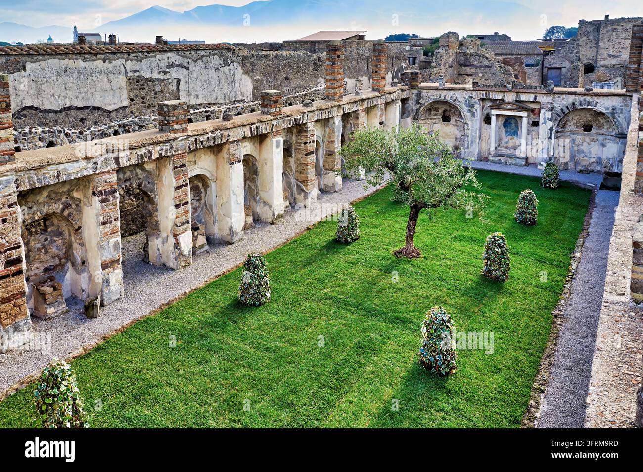 Neugepflanzter Innenhof mit Rasen, Säulengang und Ädikulenschrein inmitten der ausgegrabenen Ruinen von Pompeji nahe Neapel, Kampanien, Süditalien Stockfoto