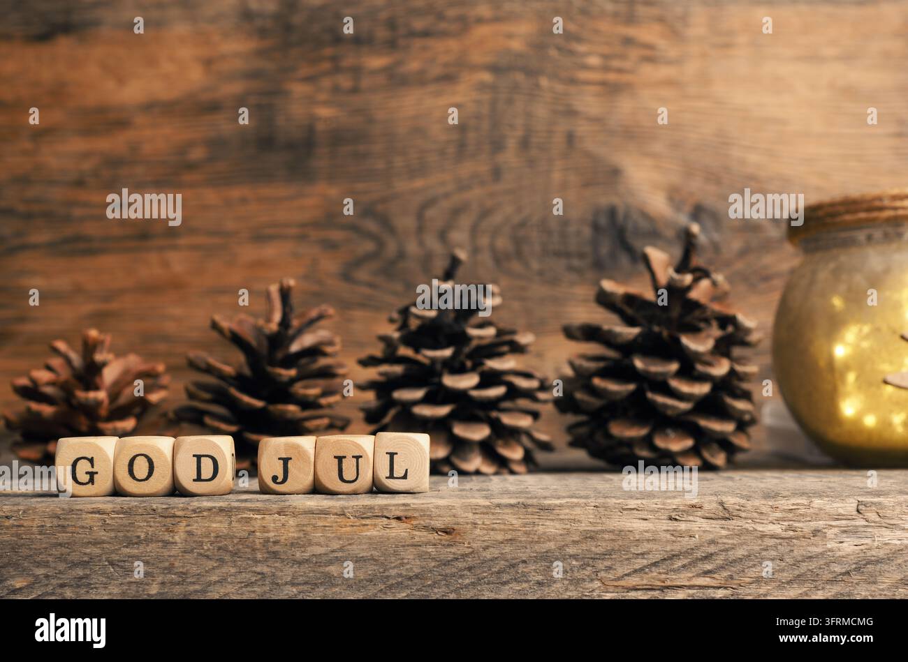Kleiner Holzblock mit den Worten God Jul und Tannenzapfen auf einem Holzhintergrund, skandinavisches Frohes Fest Stockfoto