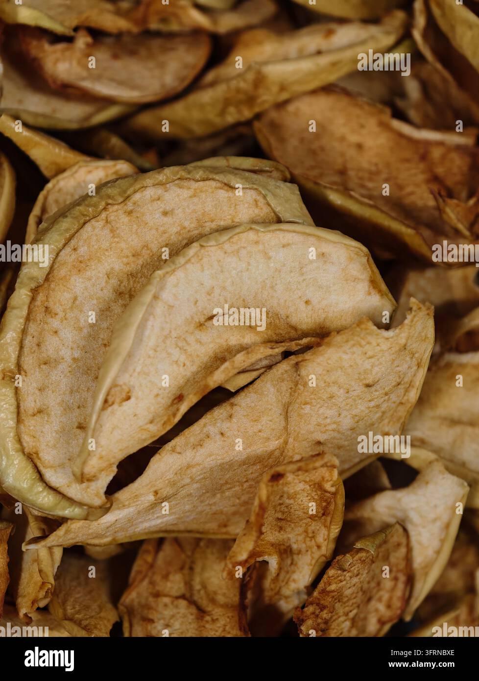 Nahaufnahme von getrockneten Apfelscheiben, die aufeinander gestapelt sind und eine runzelige Textur, hellbeiges Fleisch, gebräunte Ränder und gekräuselte Schalen unter weichem warmem Licht zeigen Stockfoto