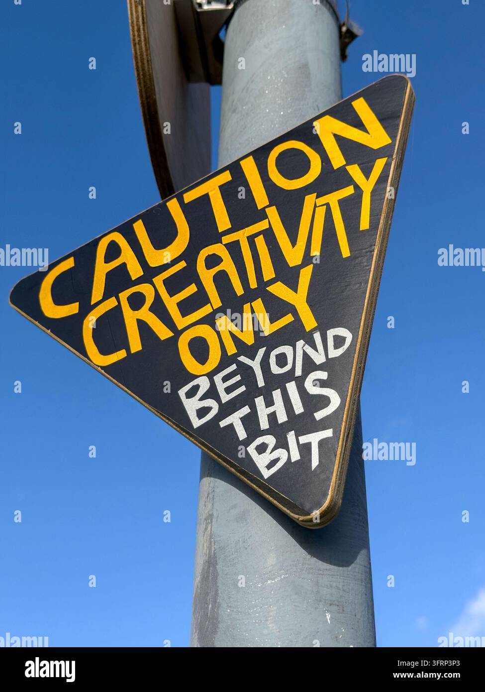 dreieckiges schwarz-gelbes Warnschild auf einem Pfahl steht "Kreativität nur jenseits dieses Punktes" Stockfoto