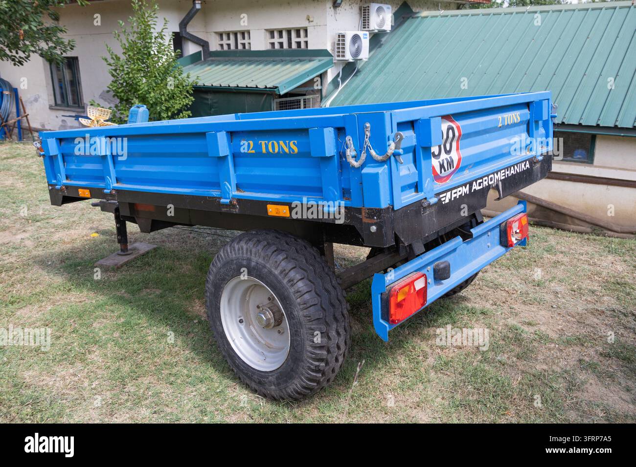 24. Juli 2026, Belgrad, Serbien: Leerer blauer Bauerntrailer ruht auf trockenem Gras und wartet auf landwirtschaftliche Nutzung oder Transportarbeit in einer Außeneinrichtung Stockfoto