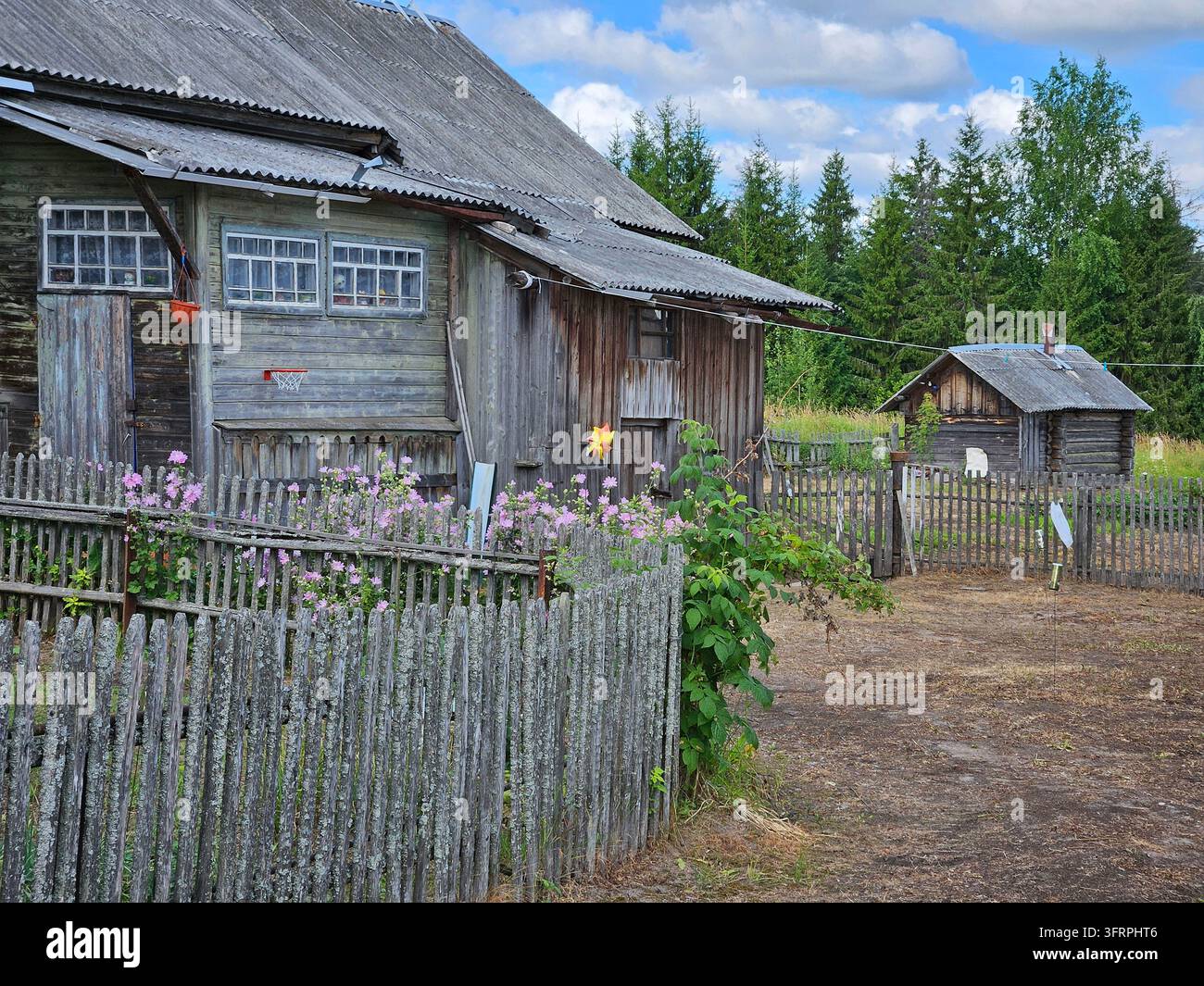 Haus mit einem Zaun und einem Schuppen. Der Zaun ist aus Holz und hat Blumen, die daran wachsen, in einem verlassenen Dorf Stockfoto