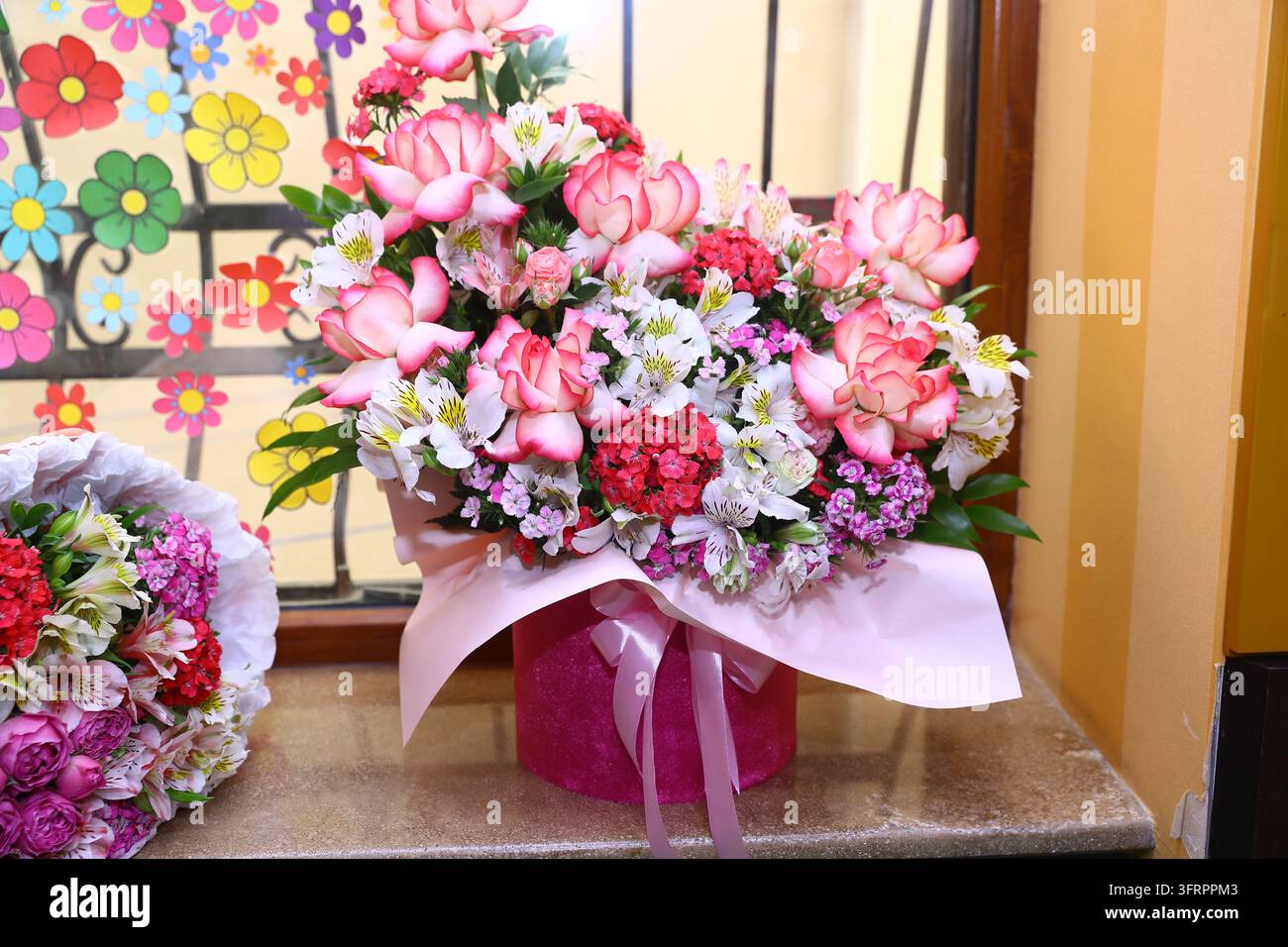 Schönes Blumenarrangement mit pinken Rosen und weißen Alstroemerien in einer runden pinken Schachtel auf einer Fensterbank. Die helle Blumenkomposition schafft Stockfoto