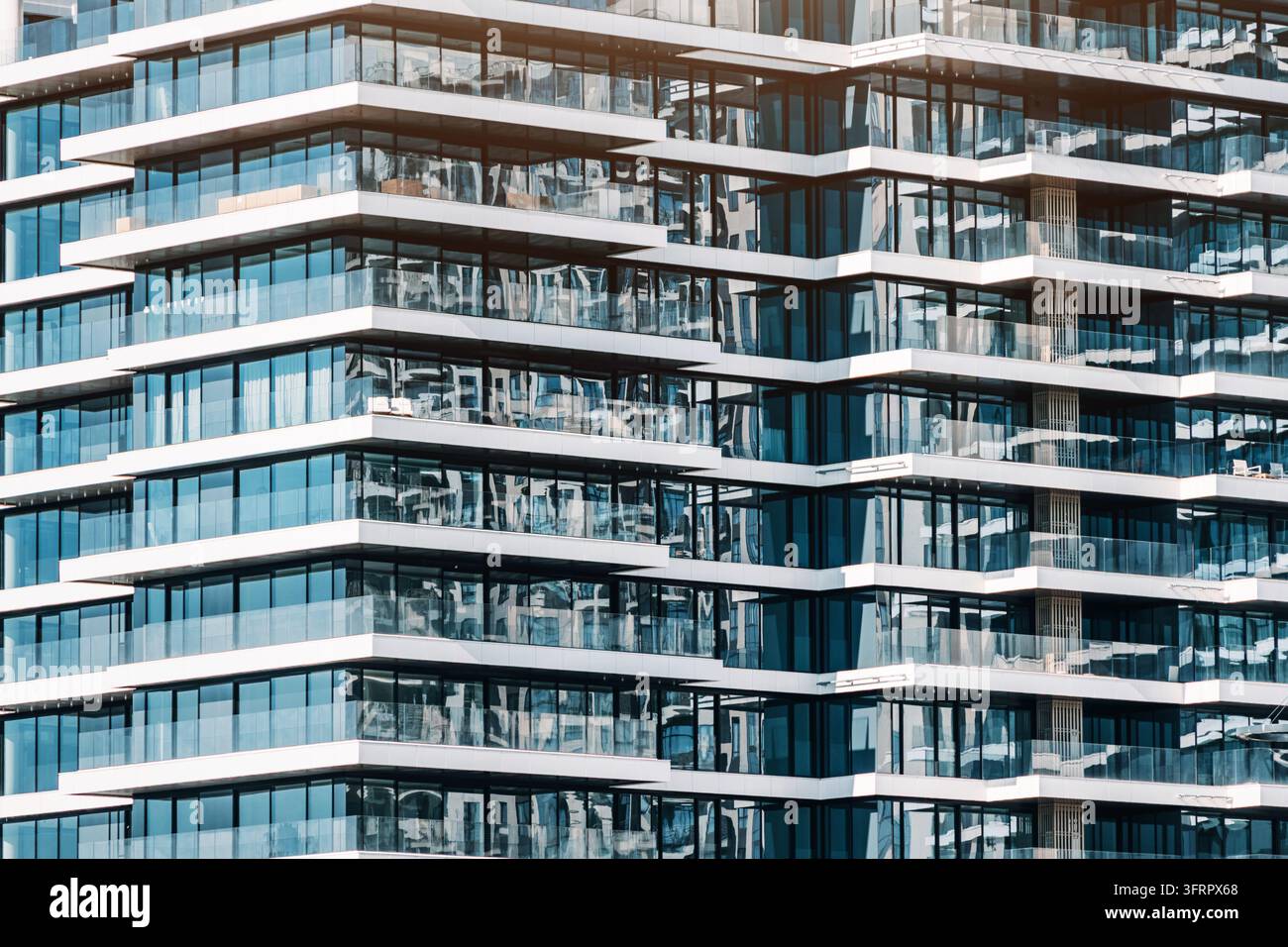 Moderner Hochhaus-Wohngebäude zeigt eine geometrische Fassade mit zahlreichen Glasfenstern und Balkonen, die den Himmel reflektieren Stockfoto