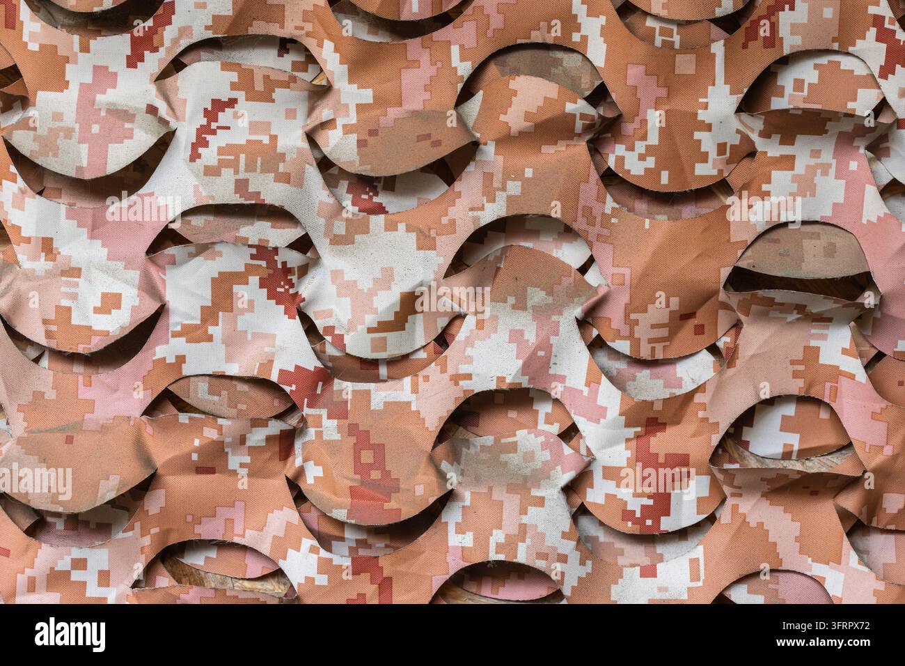 Eine Nahaufnahme von Wüstendigital-Tarnnetzen. Der Stoff weist ein welliges, gestanztes Netzmuster in den Farben Beige, Braun und Sand auf und dient als Tac Stockfoto