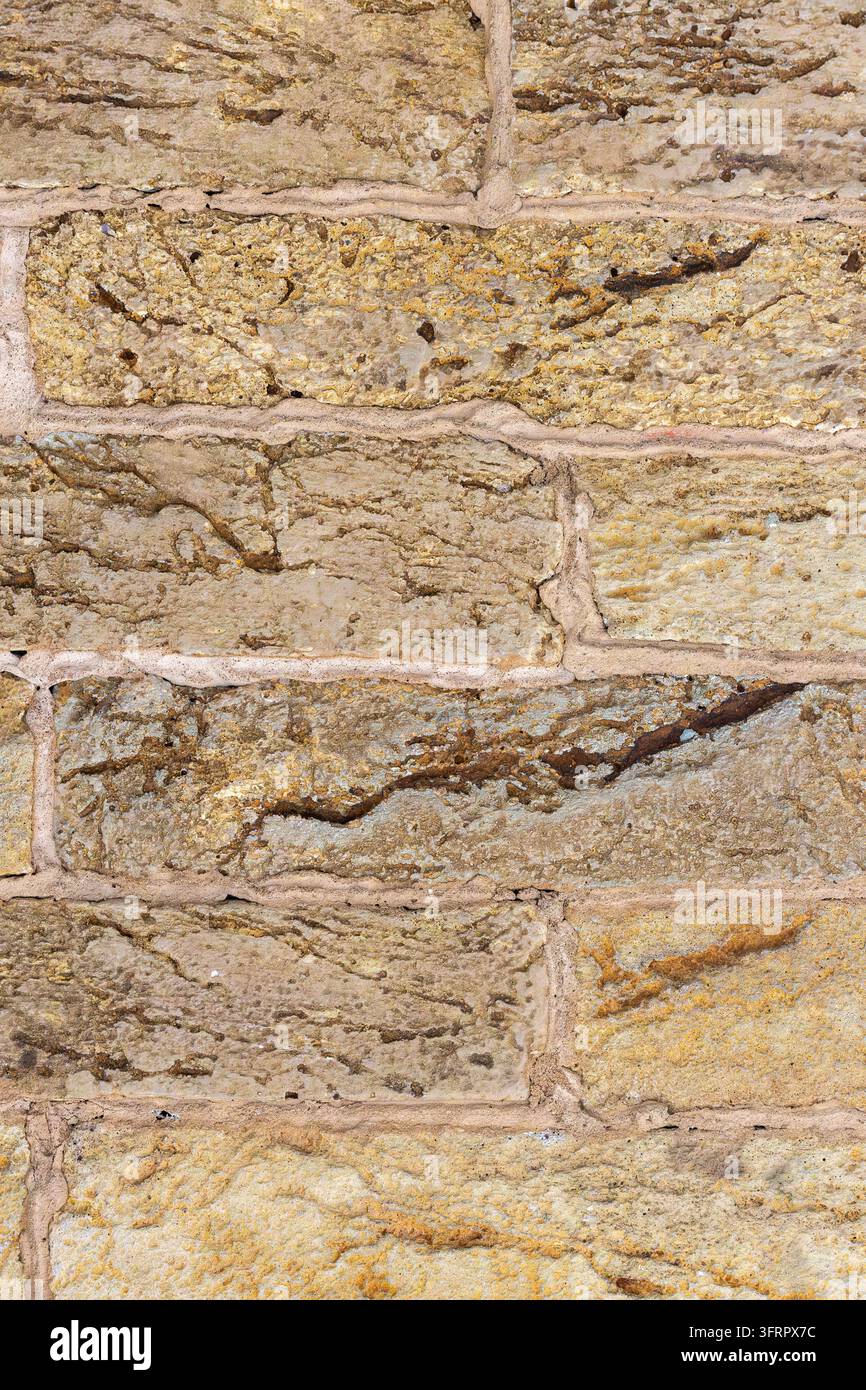 Eine detaillierte Nahaufnahme einer rauen, verwitterten Ziegelwandoberfläche, die deutliche Texturvariationen, Risse und hellfarbige Mörtelnahtverbindungen zeigt, in einer Stockfoto