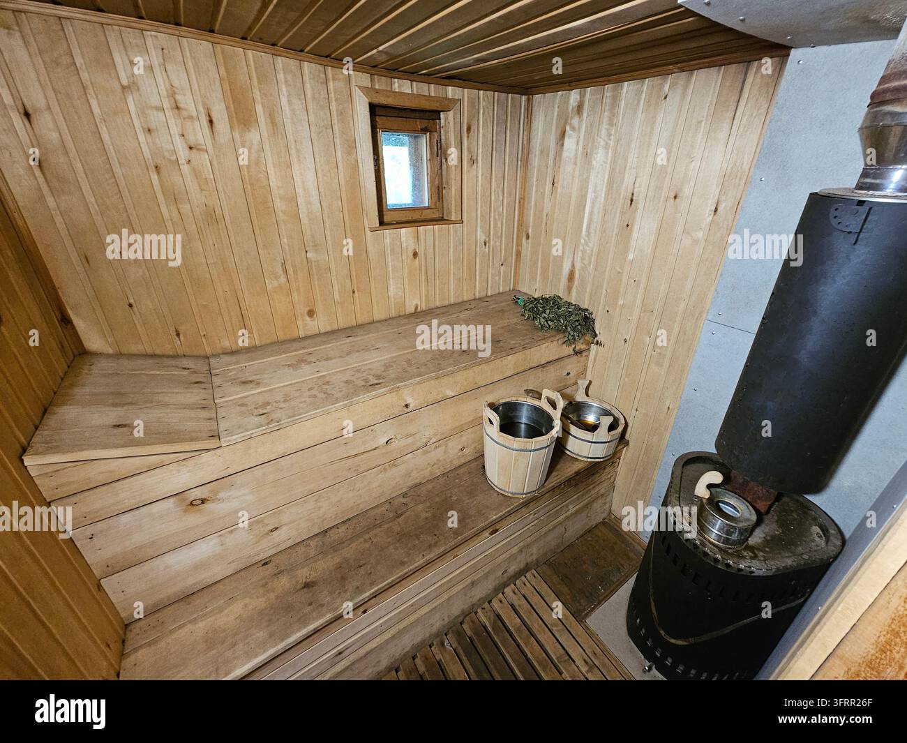 Kleine Saunaroom mit einem Holzofen und einem Fenster. Es stehen zwei Eimer auf dem Boden Stockfoto