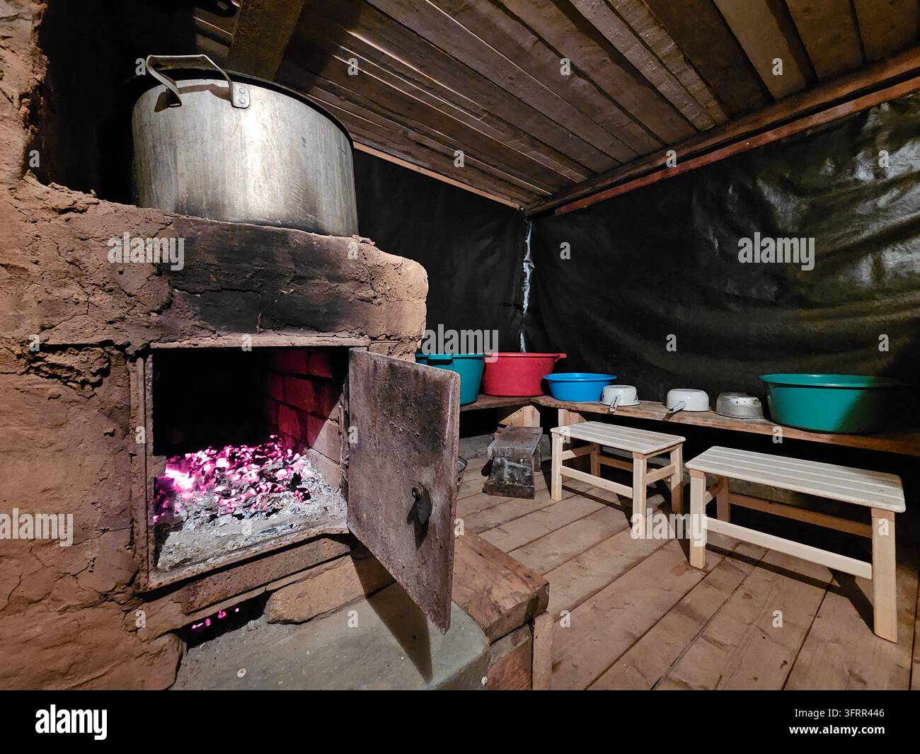 Holzofen mit einem Topf darauf. Es stehen mehrere Schüsseln und ein paar Flaschen auf dem Boden in der Banya-Sauna Stockfoto