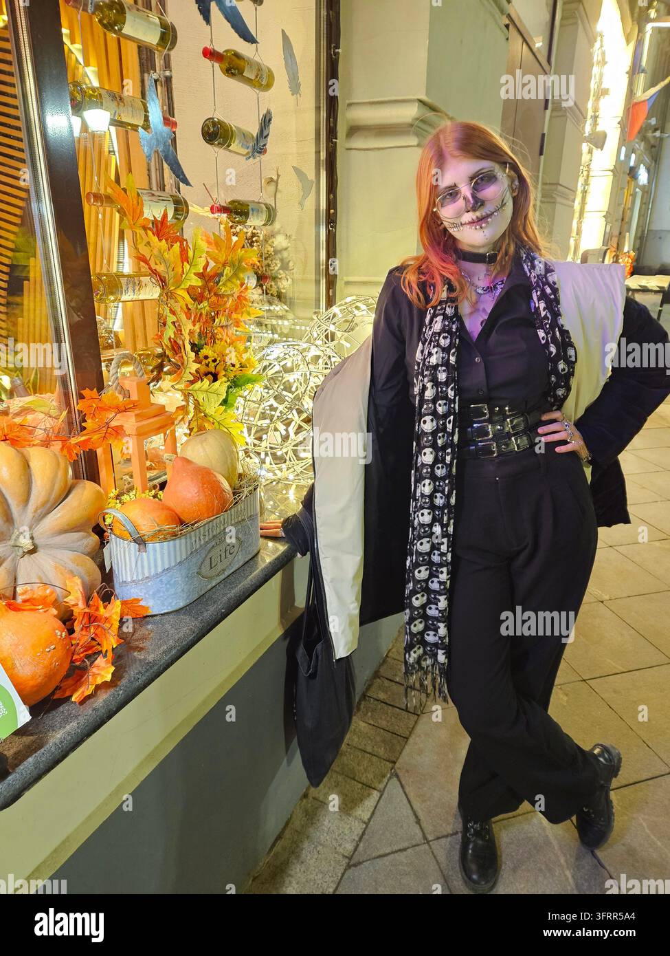 Frau in einem schwarzen Kleid und einem schwarzen Schal steht vor einem Fenster mit einem Kürbis und einer Kürbislaterne Stockfoto
