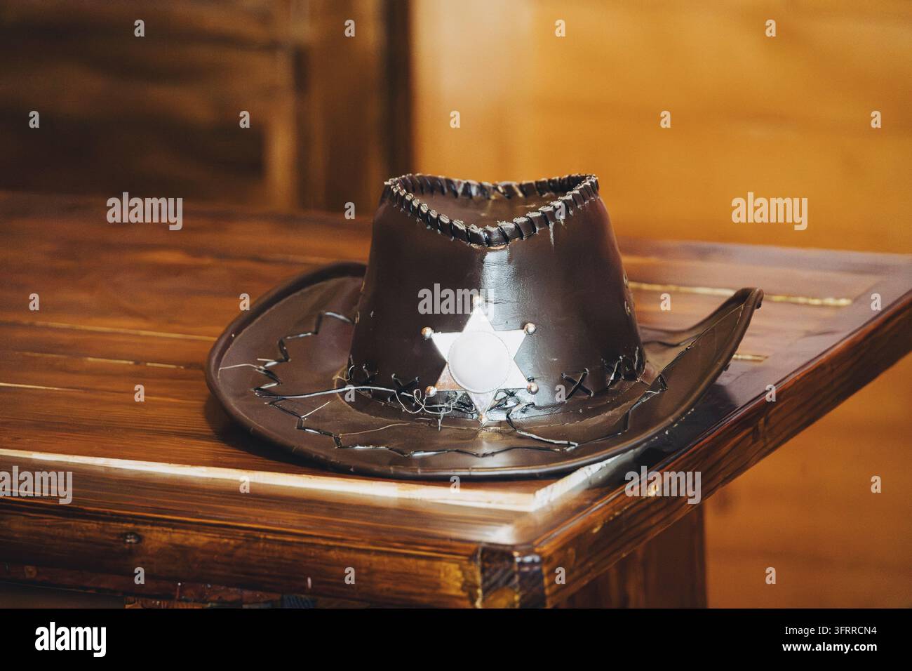 Wild-West-Konzept: dunkler Ledersheriffhut mit Sternabzeichen, der auf einem rustikalen Holztisch ruht. Stockfoto