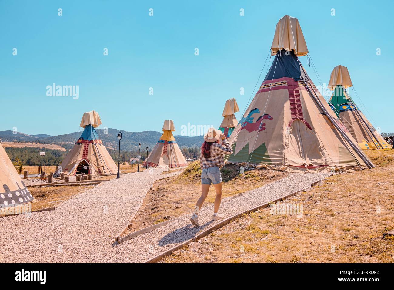17. August 2026, Zlatibor, El-Paso-Themenpark, Serbien: Frau geht in ein Tipi-Lager mit Bergkulisse. Western-Erbe-Glamping-Konzept. Stockfoto