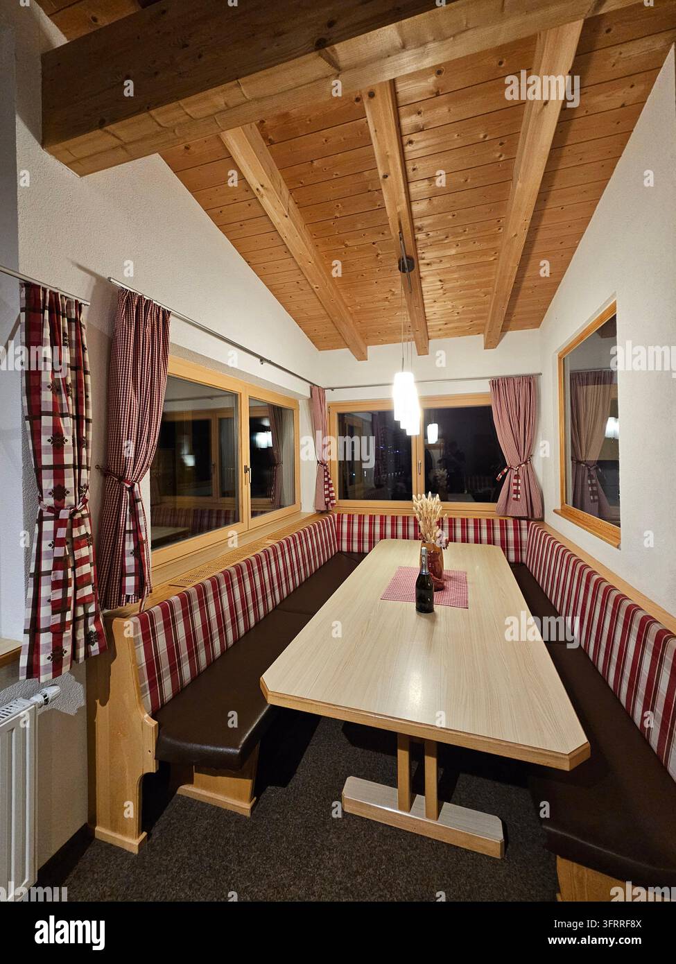 SOELDEN - JAN, 11 2025: Ein holzernes Esszimmer mit einem langen Tisch und einer Bank. Der Tisch ist mit einer Flasche Wein und einer Vase gedeckt. Der Raum hat eine gemütliche und einladende Atmosphäre Stockfoto
