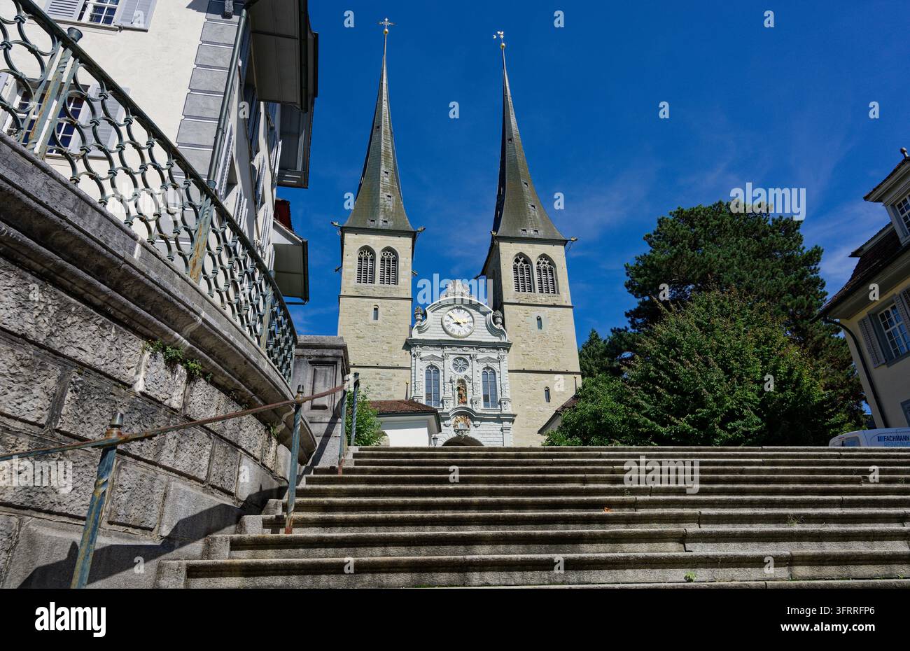 Breite Steinstufen führen hinauf zu den beiden spitzen Turmspitzen und der Uhrfassade der Hofkirche in Luzern Stockfoto