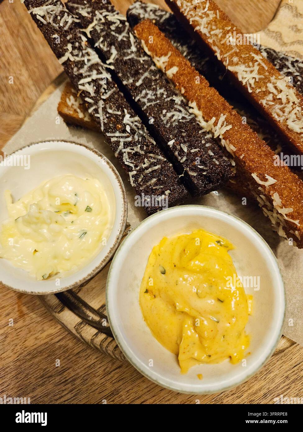 Ein Teller mit Brot und zwei verschiedenen Saucen, von denen eine gelb ist. Der Teller steht auf einem Holztisch Stockfoto