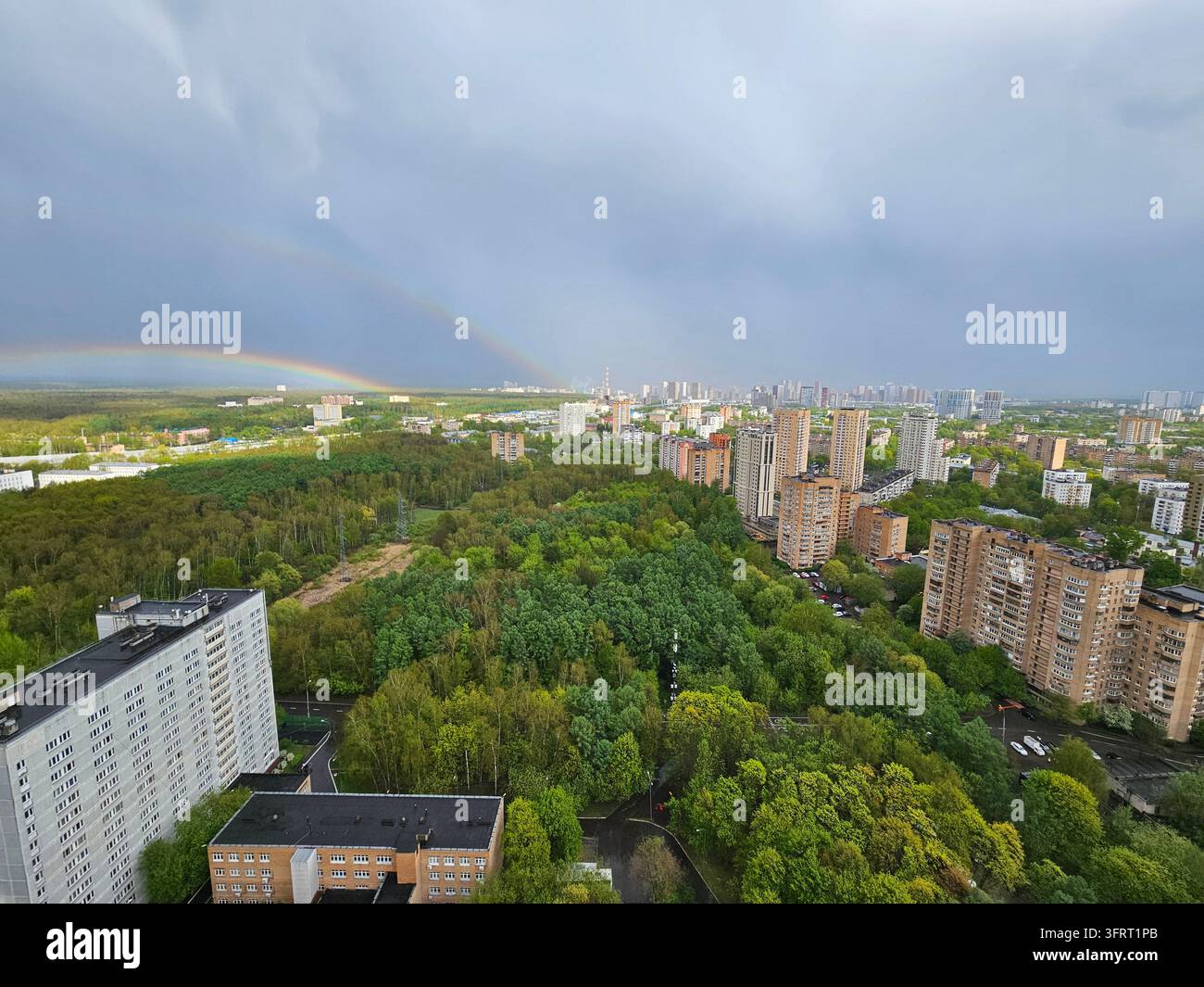 Ein Regenbogen ist am Himmel über einer Stadt sichtbar. Die Stadt ist voller hoher Gebäude und Bäume Stockfoto