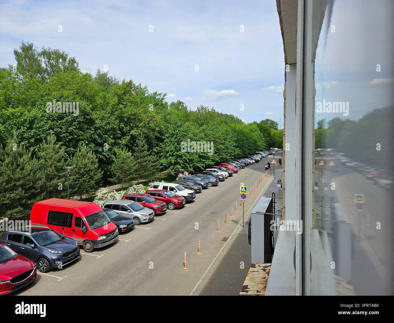 Parkplatz mit vielen Autos und einem Van. Der Van ist rot. Es sind viele Autos auf dem Parkplatz geparkt Stockfoto
