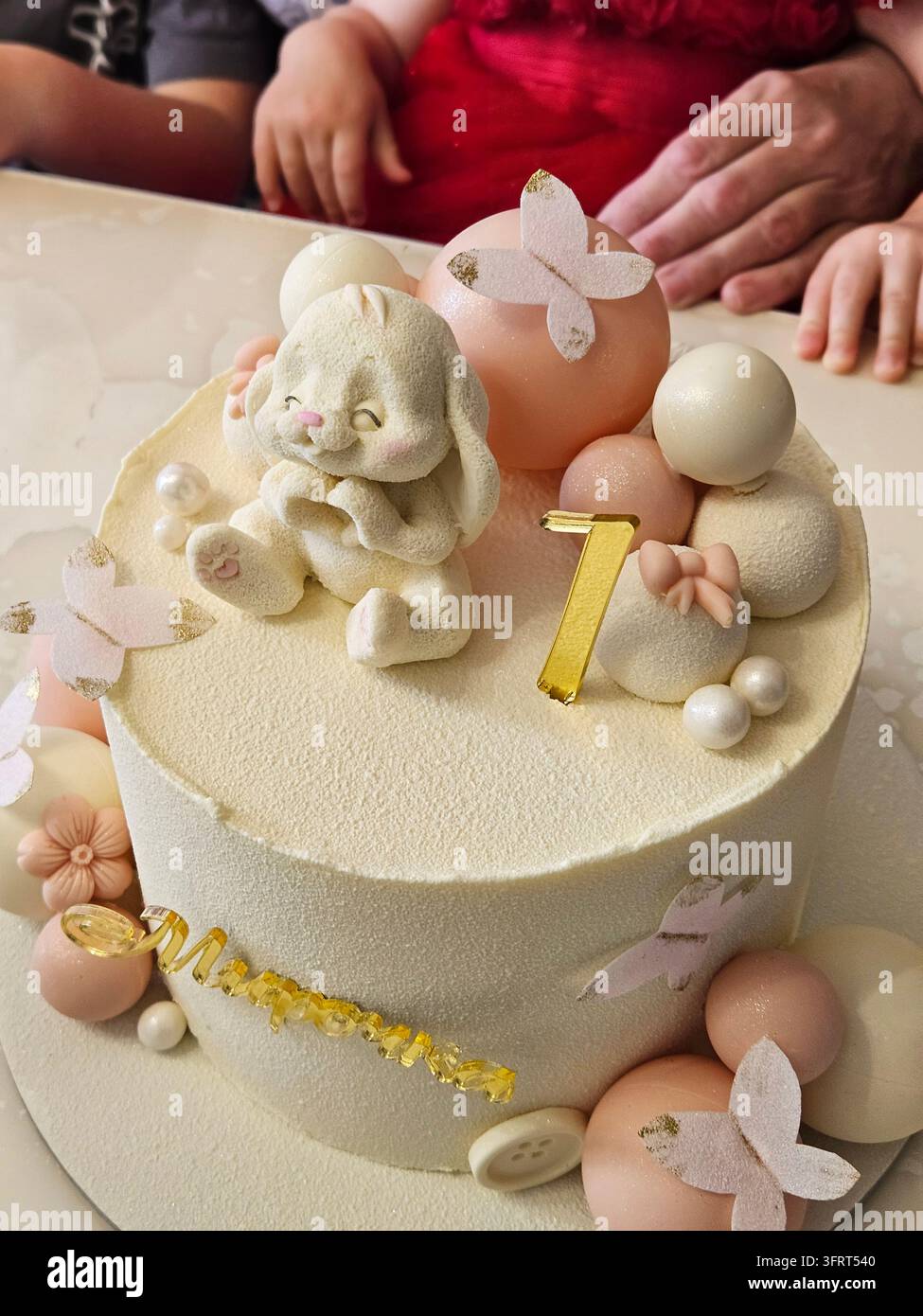 Kuchen mit einem Kaninchen oben und der Nummer 1 darauf. Der Kuchen ist mit Schmetterlingen und anderen kleinen Dekorationen mit dem Text Babynamen Mirochka zum Geburtstag geschmückt Stockfoto