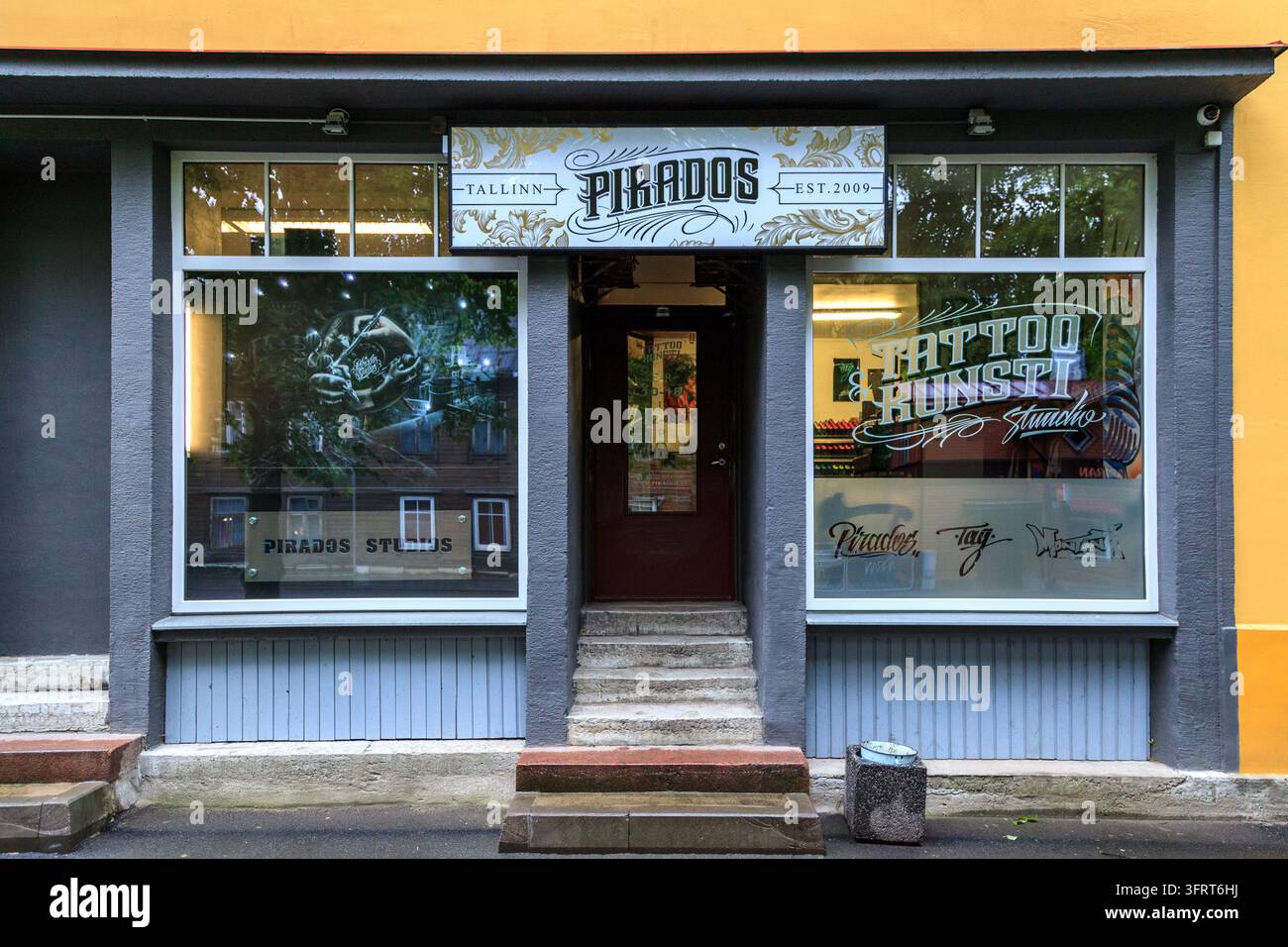 Schaufenster des Pirados-Tattoostudios in Tallinn, Estland, mit dekorativem Schild, Fensterbeschriftung und Kunstwerken, einer zentralen Tür und Eingangstreppe Stockfoto