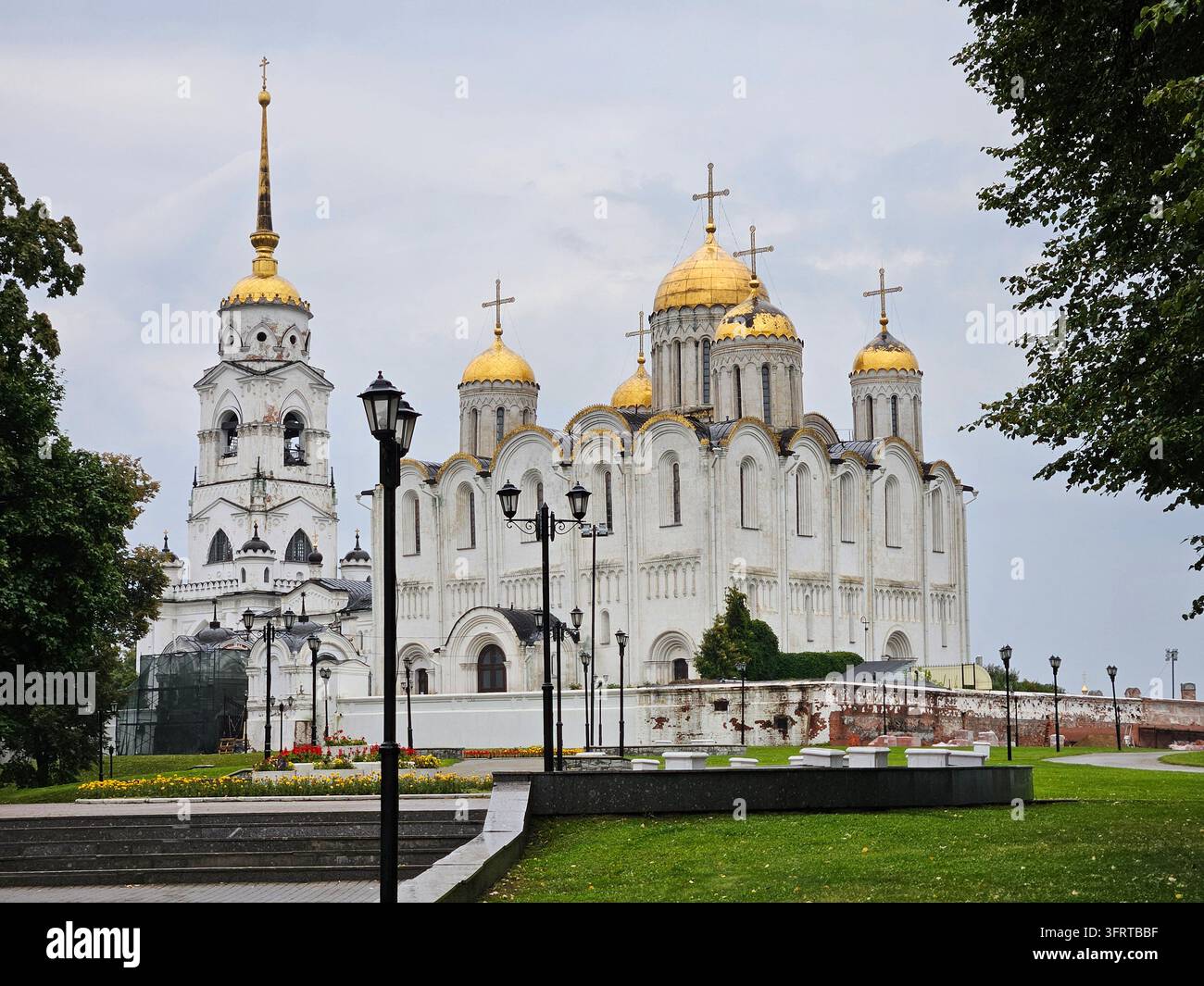 Große weiße Kirche mit goldenen Kuppeln und einem hohen Turm. Die Kirche ist von einem üppigen grünen Park in der Stadt Wladimir umgeben Stockfoto