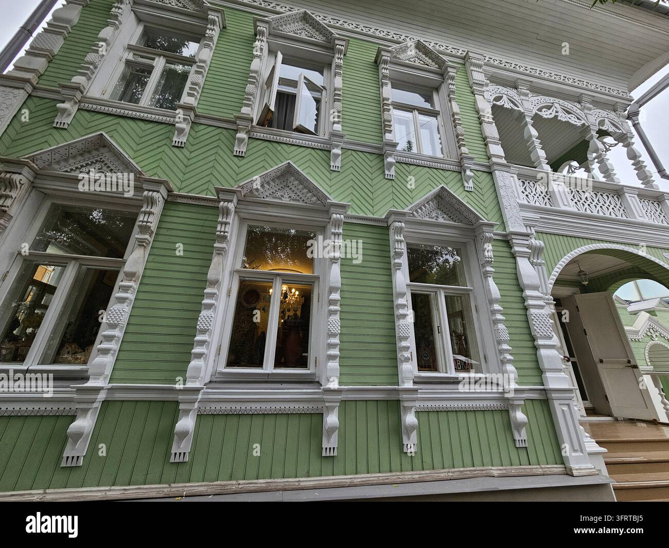 Großes grünes Haus mit weißer Zierleiste und einer weißen Tür. Das Haus hat viele Fenster und einen Balkon Stockfoto