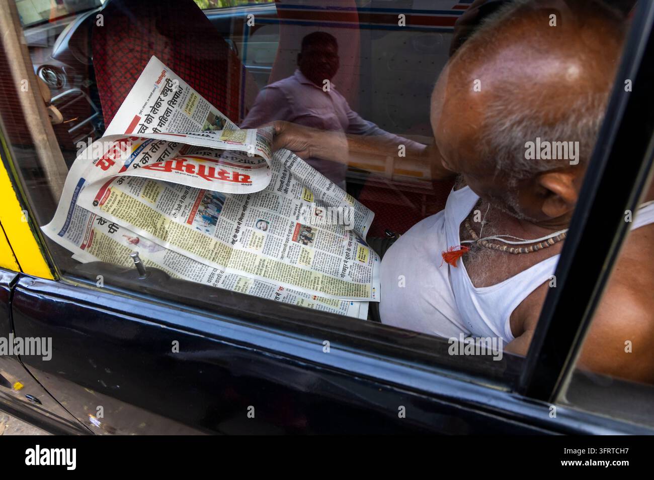Älterer Mann liest eine Hindi-Zeitung in einem schwarz-gelben Taxi mit der Reflexion eines anderen Mannes im Autofenster, Maharashtra, Mumbai, Indien Stockfoto