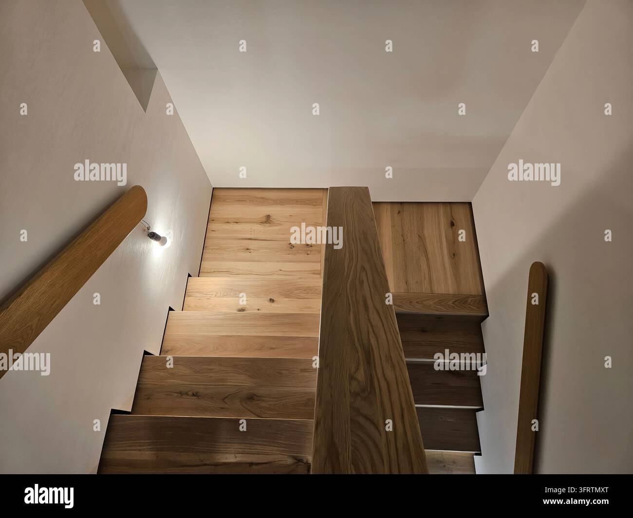 Moderne Holztreppe mit natürlicher Holzoptik. Das Licht betont klare Linien und warme Töne. Grob behauene Balken kontrastieren mit glatten weißen Wänden. Minimalistisches Design verbindet Struktur mit Raum (PR) Stockfoto
