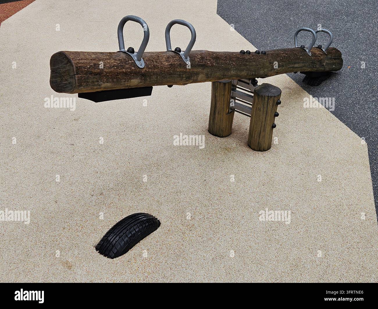 Holzschaukel mit Metallringen und schwarzem Gummipolster. Kinderspielgerät auf Kiesoberfläche. Einfaches Design für Außen Spielplätze. Natürliche Holztextur und robuste Konstruktion Stockfoto