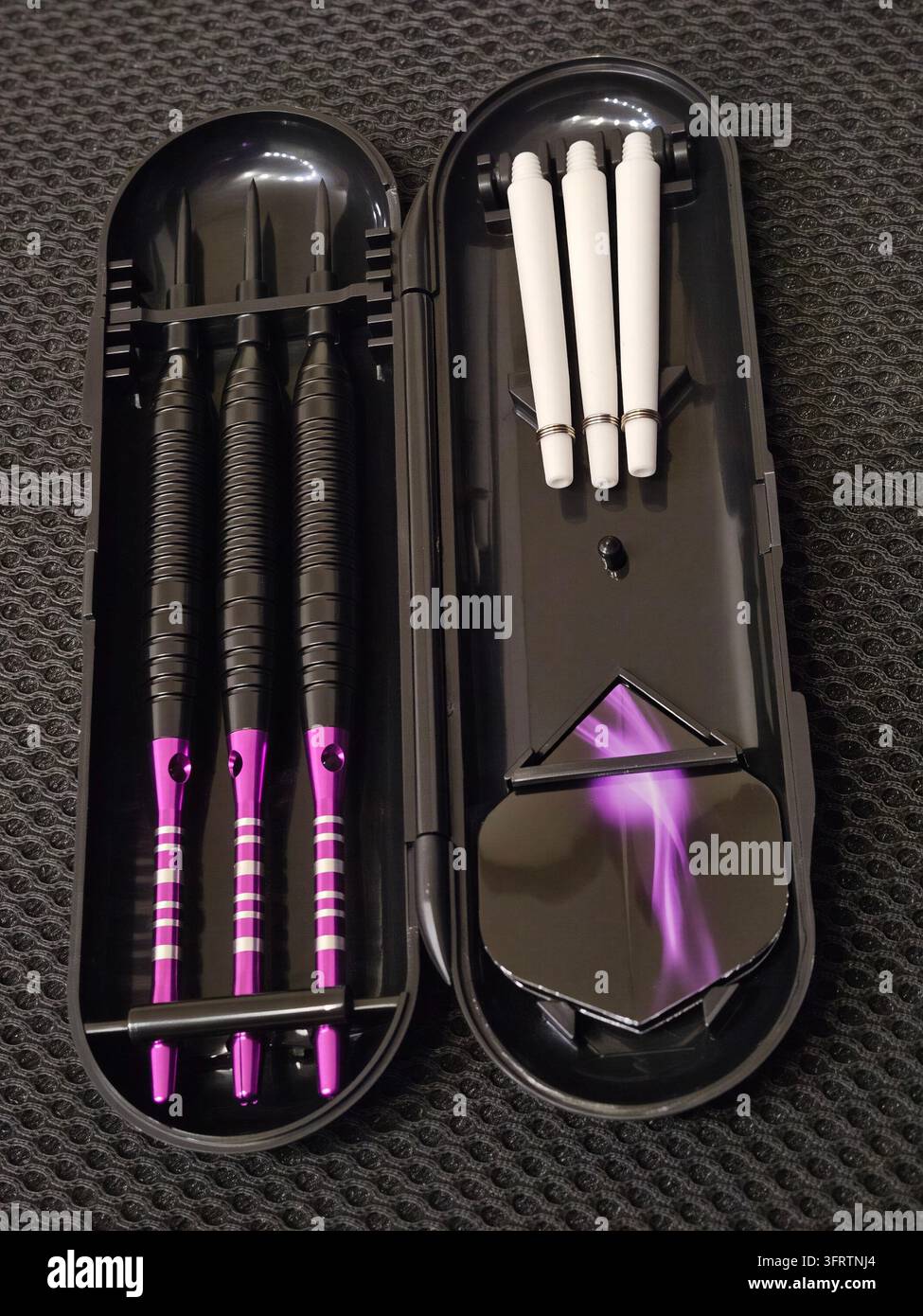 Lila Dart-Flights in schwarzem Köfferchen mit weißen Darts. Geöffneter Koffer zeigt Darts und Ablagefach. Die Darts haben schwarze Schäfte und lila Spitzen. Der Deckel des Koffers zeigt ein lila Flammen-Design Stockfoto
