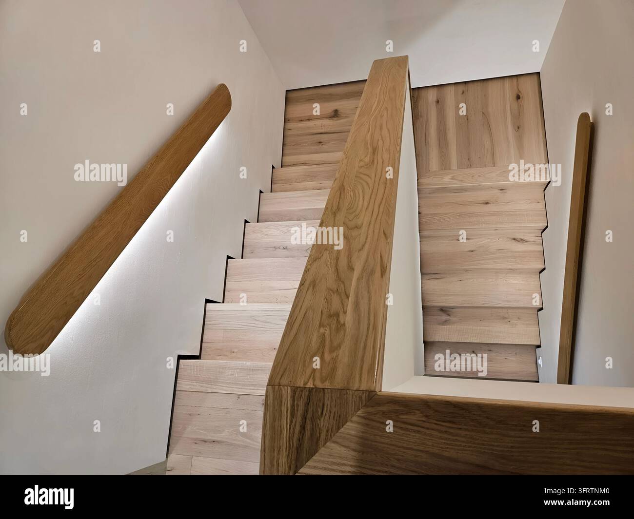 Moderne Holztreppe mit integrierter LED-Beleuchtung. Glatte Oberfläche betont natürliche Maserungen. Klare Linien definieren minimalistischen Baustil. Treppenstufen-Geländer passen zu Holztönen (PR) Stockfoto