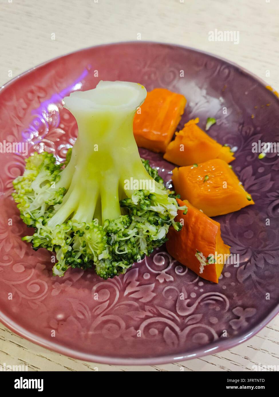 Frischer Brokkoli und Süßkartoffel-Würfel auf einem gemusterten Teller. Lebendige Grüntöne kontrastieren mit warmen Orangetönen. Einfaches, elegantes Gericht, bereit für zwangloses oder gehobenes Essen. Natürliches Licht hebt die Texturen hervor Stockfoto