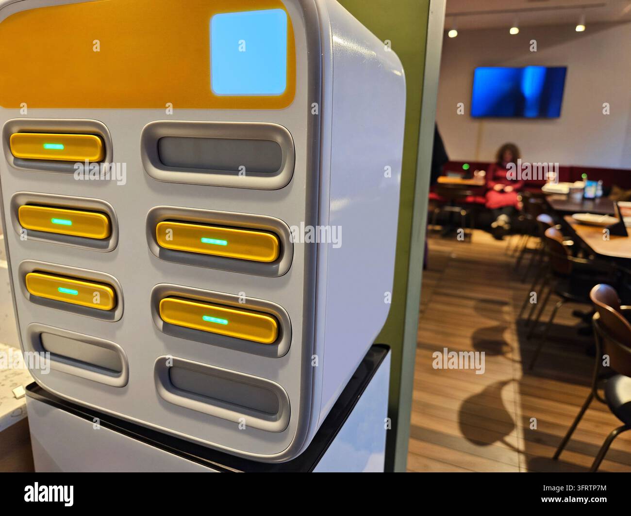 Moderne elektrische Akkuladeeinheit in einem gewerblichen Café. Mehrere Steckplätze mit sichtbaren Anzeigelampen. Im Hintergrund sind Innenbestuhlung und Ambientebeleuchtung zu sehen Stockfoto