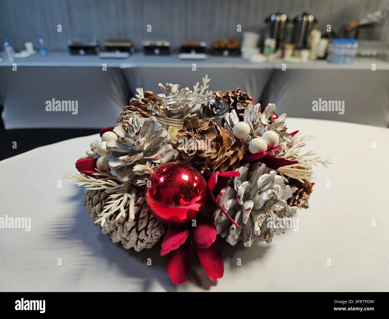 Festlicher Feiertags-Tischschmuck mit Tannenzapfen und roter Kugel. Silber- und Goldtöne schaffen eleganten Wintercharme. Rote Beeren und zartes Laub verleihen einen lebendigen Kontrast Stockfoto