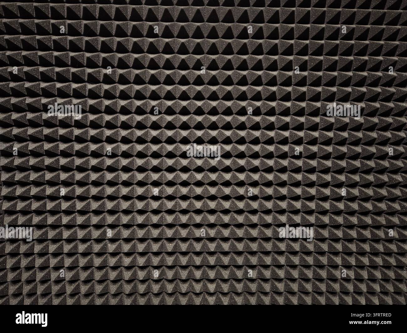 Schwarzer Schaum mit sich wiederholenden dreieckigen Spitzen. Textur sorgt für akustische Absorption. Gleichmäßiges Muster dominiert das gesamte Bild. Ideal für Hintergründe oder Designelemente. Hoher Kontrast auf dunkler Oberfläche Stockfoto