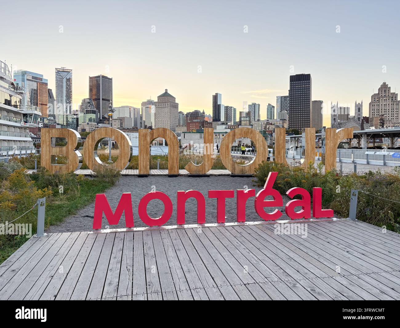 Schild mit der Aufschrift „Bonjour Montreal“ im alten Hafen von Montreal, mit großen Holz- und roten Buchstaben und der Skyline der Stadt im Hintergrund. Stockfoto