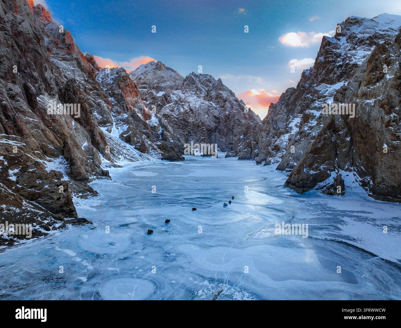 Weite Perspektive einer eisigen gefrorenen Wasseroberfläche, flankiert von schroffen Bergen in der Dämmerung Stockfoto