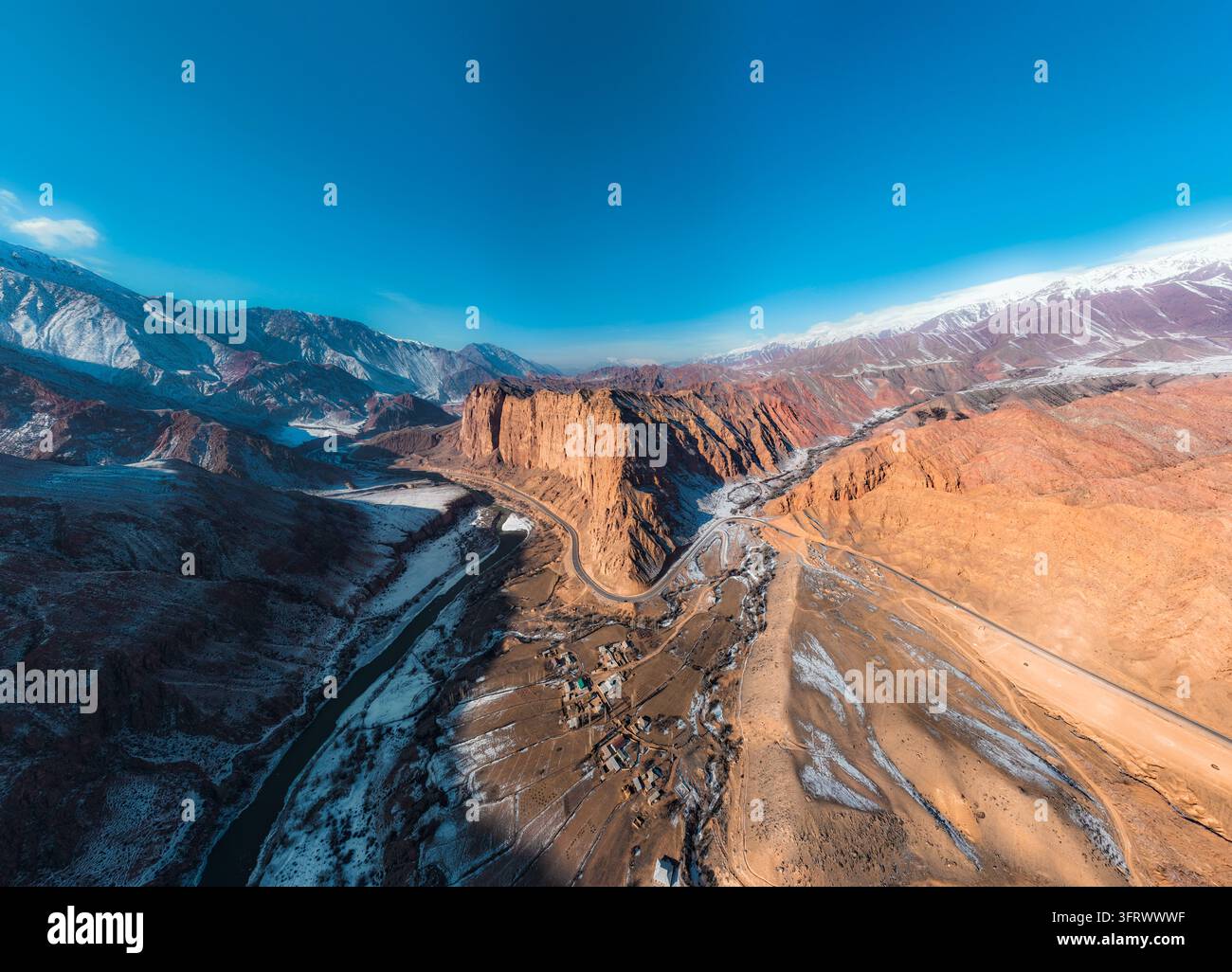 Weitläufiges Luftpanorama einer sich windenden Straße, eines Flusstals, roter Klippen und schneebedeckter Berge Stockfoto