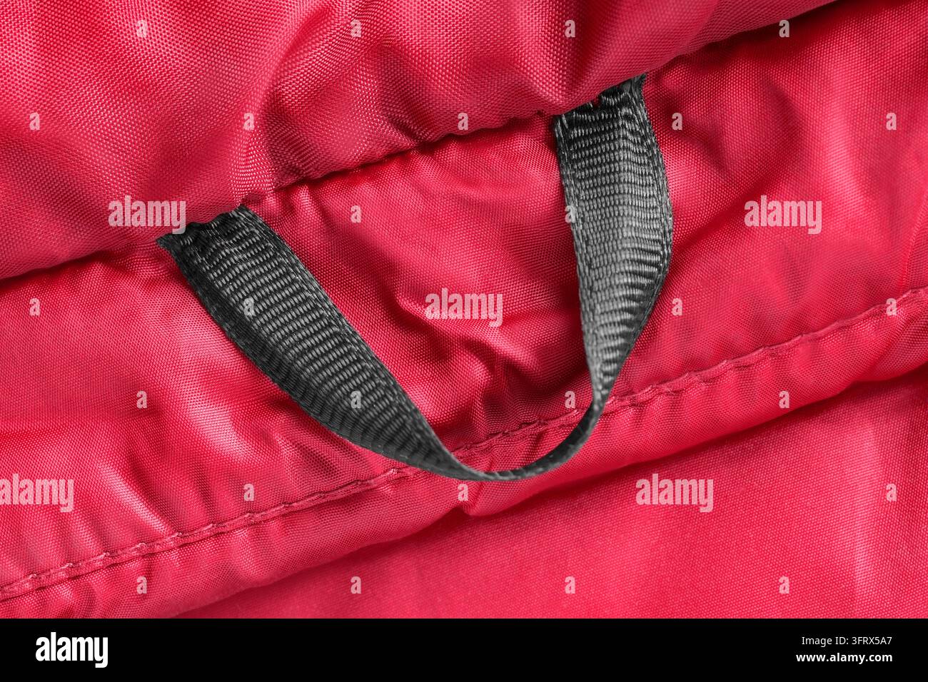 Schwarze Stoffjacke mit Aufhängung auf rotem wasserdichtem Stoff, Nahaufnahme als Hintergrund Stockfoto