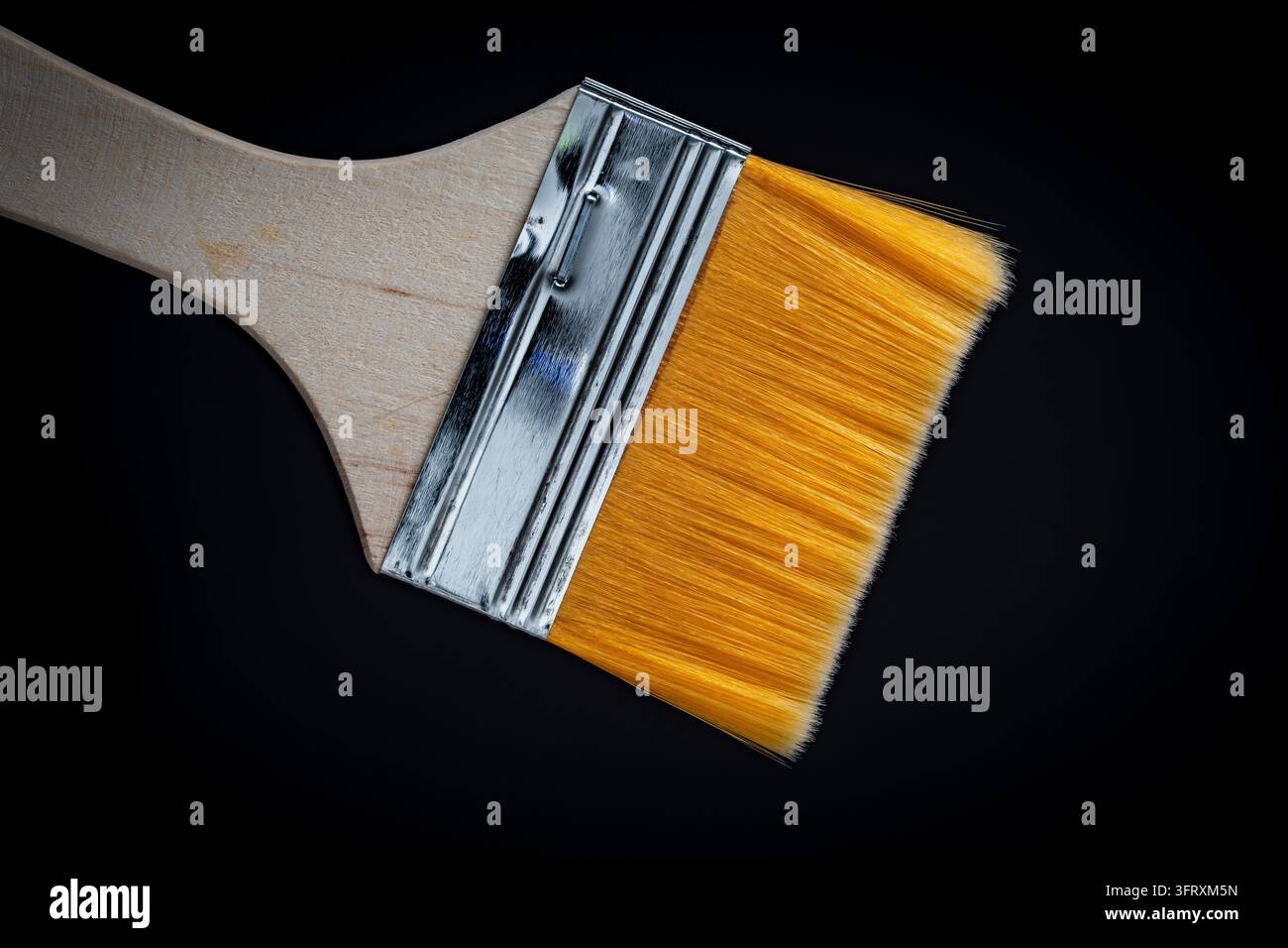 Orangefarbener Pinsel mit Holzgriff, Nahaufnahme auf schwarzem Hintergrund. Pinsel mit gelben Kunstborsten und Metallzwinge. Konzept der Renovierung Stockfoto