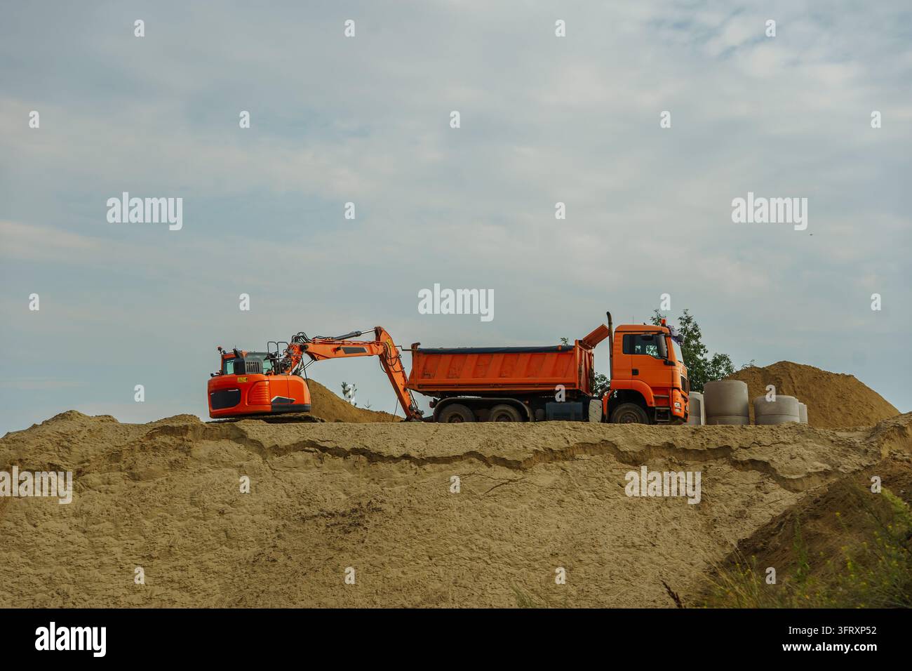 Oranger Bagger und Kipplaster auf einer sandigen Baustelle. Schwere Industrieausrüstung führt Erdbewegungen für die Infrastrukturentwicklung durch Stockfoto